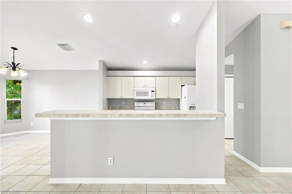 Kitchen featuring light cabinetry, a white microwave, and an electric range, complemented by a tiled backsplash
