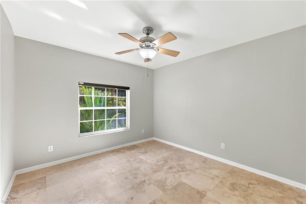 Spacious room featuring tile flooring, a window with exterior foliage, a ceiling fan with light fixture, and neutral painted walls