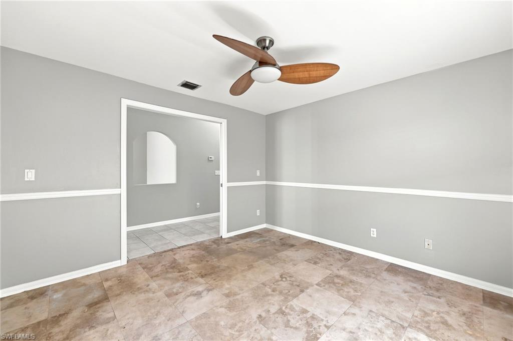 Spacious room featuring neutral wall tones with decorative chair rail molding, large format tile flooring, and a ceiling fan with integrated lighting