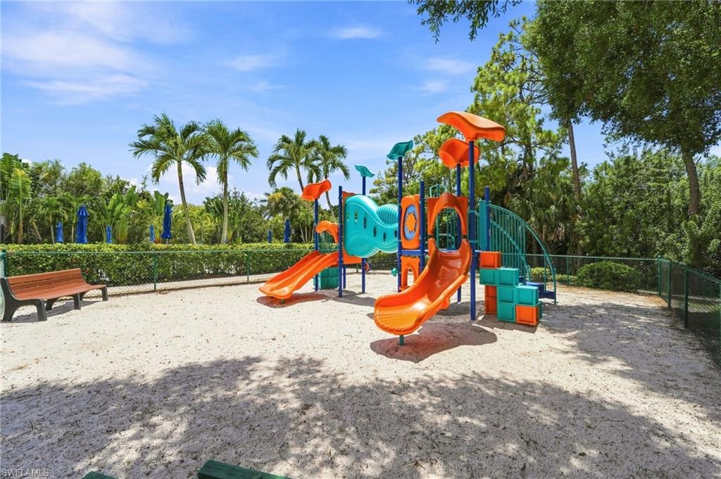 Recreational playground featuring a multi-level play structure with orange and turquoise components, dual slides, climbing elements, and sand surfacing