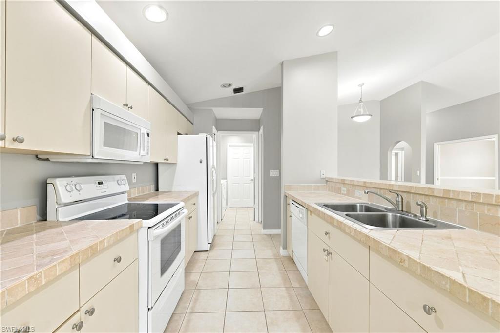 Galley kitchen featuring light cabinetry, tile flooring, white appliances, recessed lighting, and a double basin stainless steel sink
