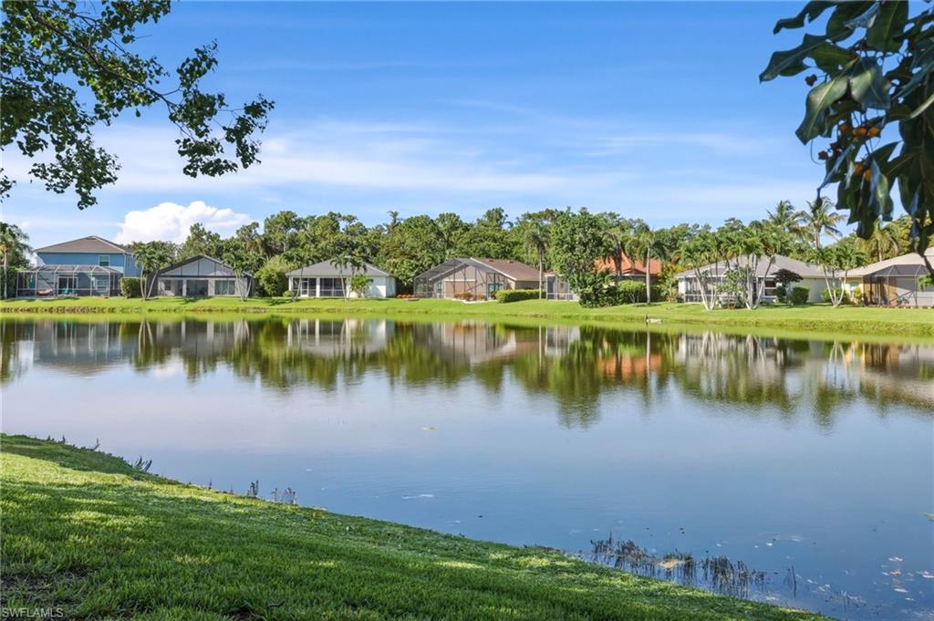 Expansive lakefront property featuring a serene water body, lush green landscaping, and mature tropical foliage