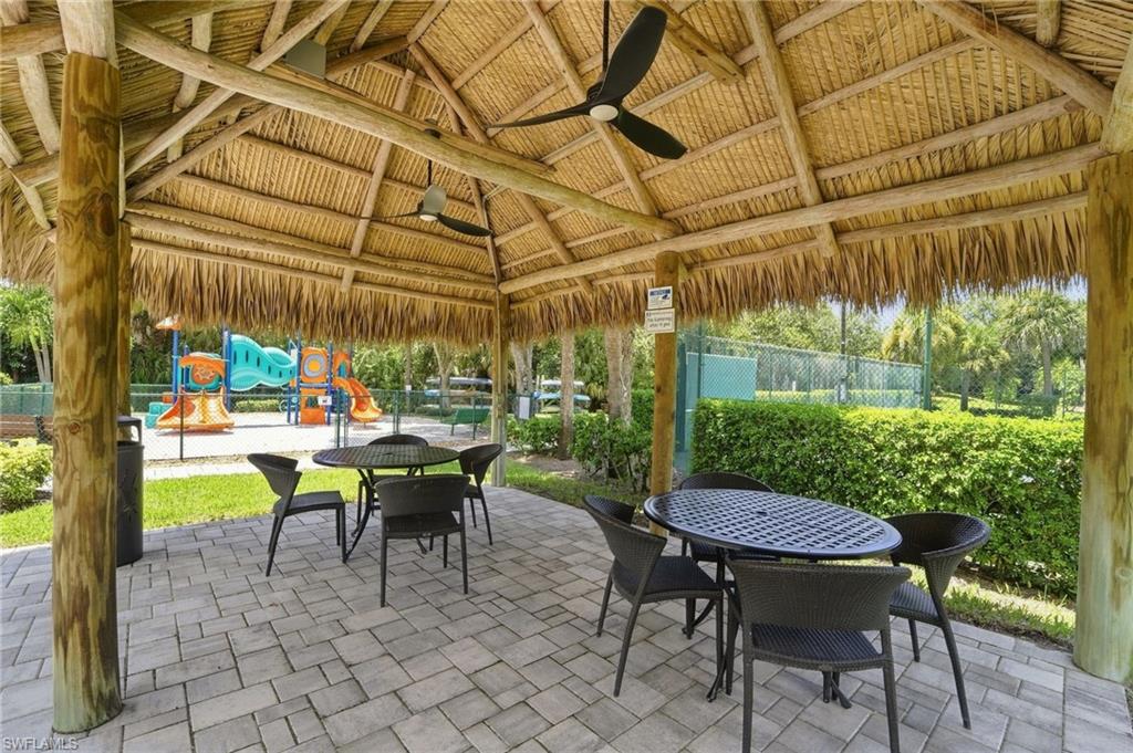 Expansive covered patio with thatch-style roof and exposed beam construction, featuring a paver stone floor and ceiling fan