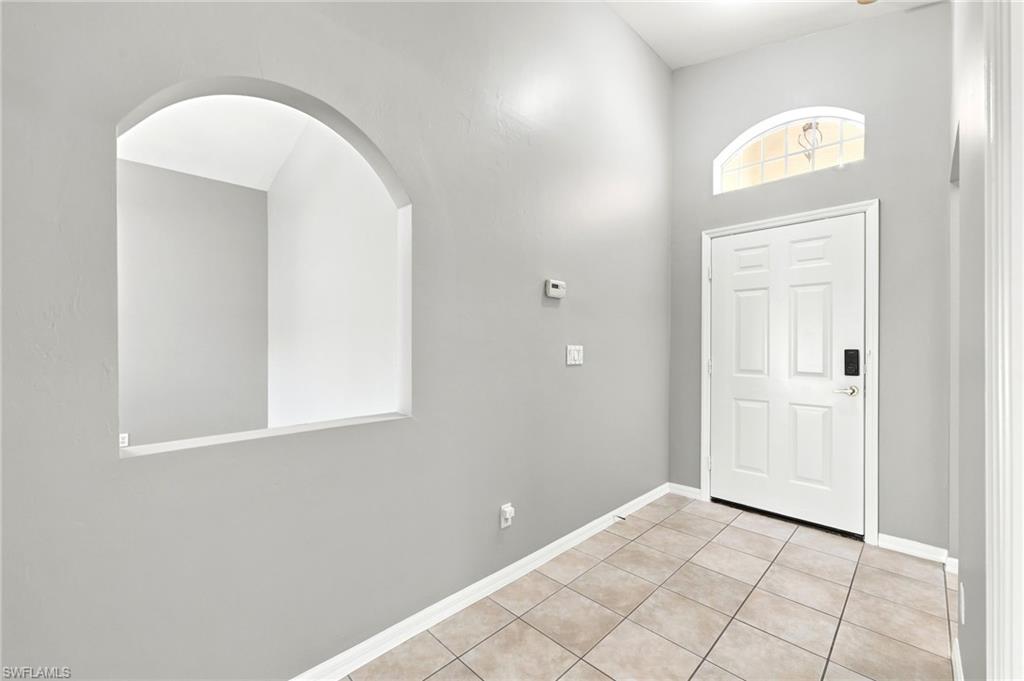Entryway featuring light-toned tile flooring, a paneled white door with smart lock, and an arched transom window