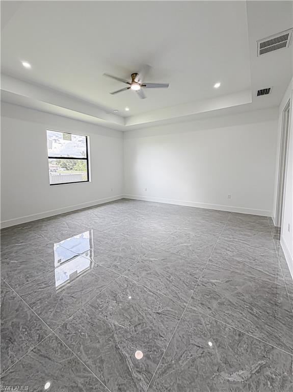Spacious room featuring large format grey tile flooring, a tray ceiling with recessed lighting, and a modern ceiling fan