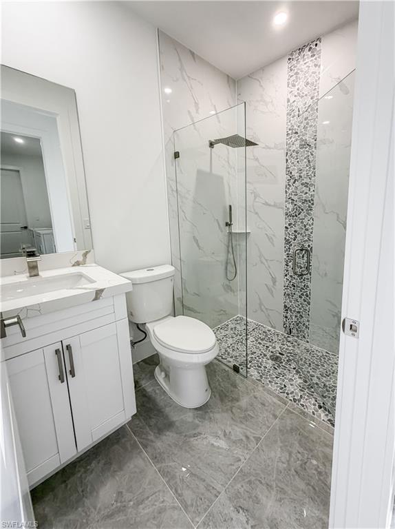 Contemporary bathroom featuring a frameless glass shower enclosure, a rain showerhead, a pebble-tiled shower floor, and a full-height marble-look tiled shower surround with a decorative mosaic accent