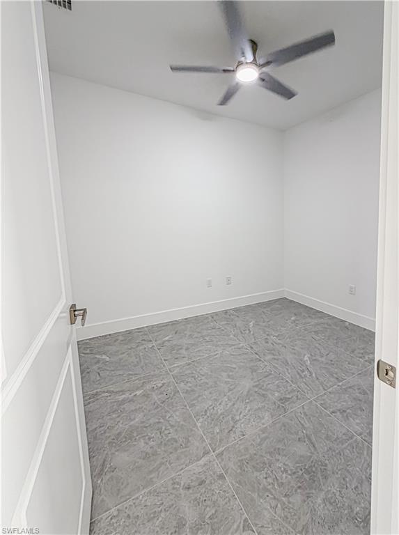Modern room featuring large format grey floor tiles, white walls, and a ceiling fan with integrated lighting