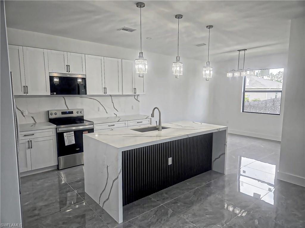 White shaker cabinetry, integrated stainless steel appliances, and a waterfall island with a fluted panel base