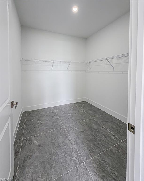 Walk-in storage space featuring grey large-format tile flooring, white wire shelving, a recessed ceiling light, and white baseboards