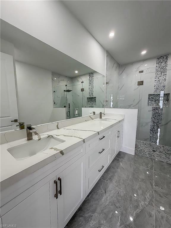 Spacious bathroom featuring a dual vanity with white cabinetry and patterned countertops, undermount sinks, and dark bronze fixtures