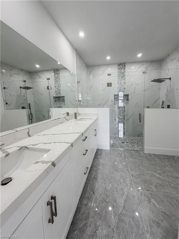 Spacious bathroom featuring a dual vanity with a white countertop and integrated sinks, extensive wall-to-wall mirror, two glass-enclosed shower stalls with rain showerheads, and large-format grey-toned floor tiling