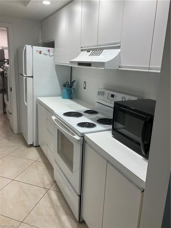 Kitchen with white electric stove, range hood, light countertops, light tile patterned floors, and white cabinetry