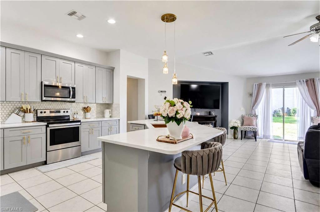Kitchen featuring light gray cabinetry, stainless steel appliances, white quartz countertops, and a honeycomb tile backsplash