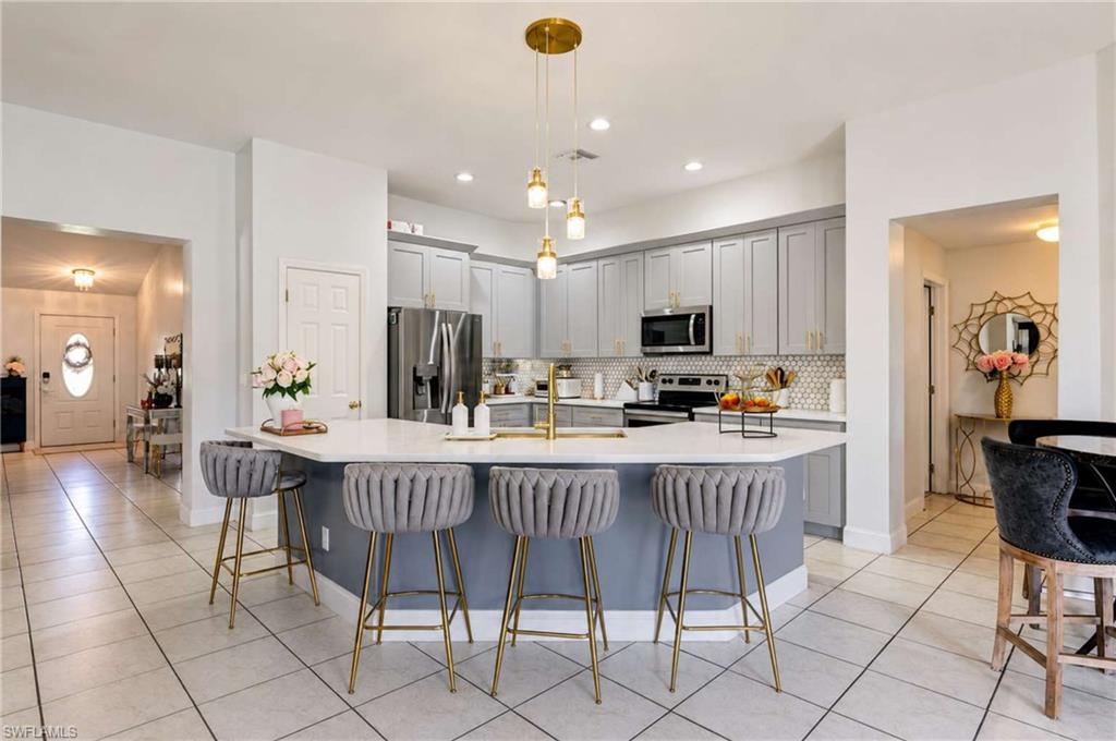 Kitchen featuring a central island with countertop seating, stainless steel appliances, a tile backsplash, light-toned cabinetry, and recessed lighting