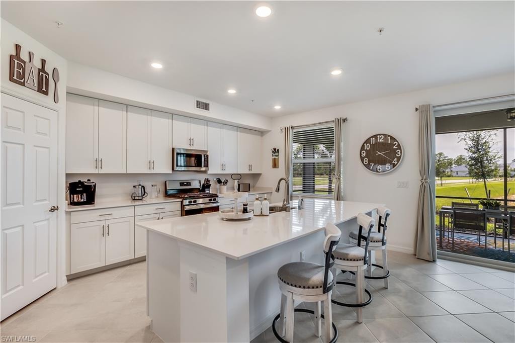 Kitchen with stainless steel appliances, a center island with sink, light tile floors, white cabinets, and a kitchen bar