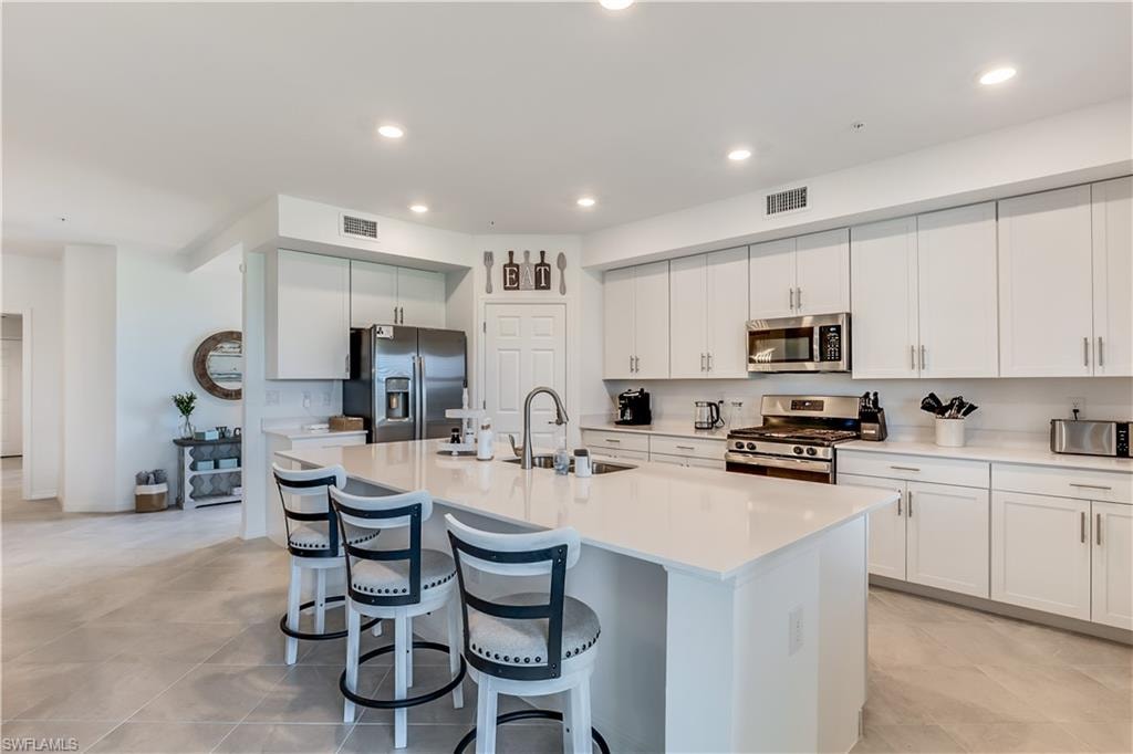 Kitchen with an island with sink, sink, white cabinetry, and appliances with stainless steel finishes