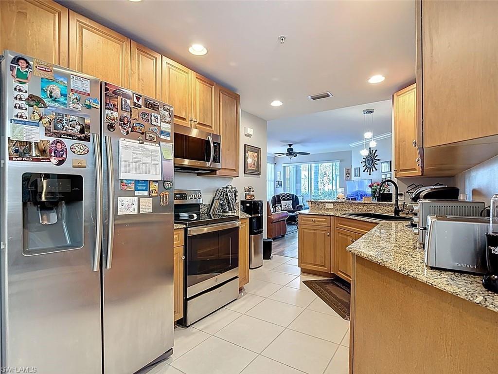 Kitchen with stainless steel appliances, light stone countertops, a peninsula, a ceiling fan, and light tile patterned floors