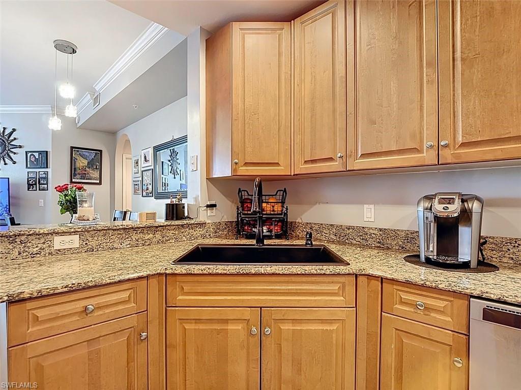 Kitchen featuring crown molding, light stone counters, arched walkways, decorative light fixtures, and stainless steel dishwasher