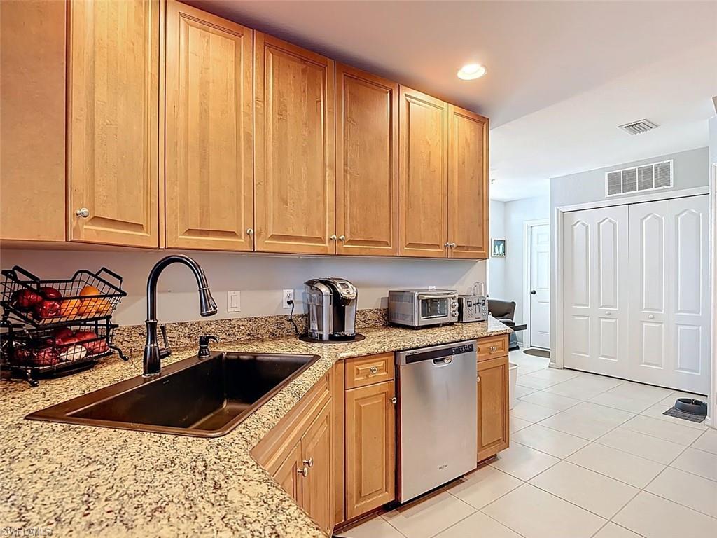 Kitchen with stainless steel dishwasher, light tile patterned flooring, light stone countertops, recessed lighting, and brown cabinetry