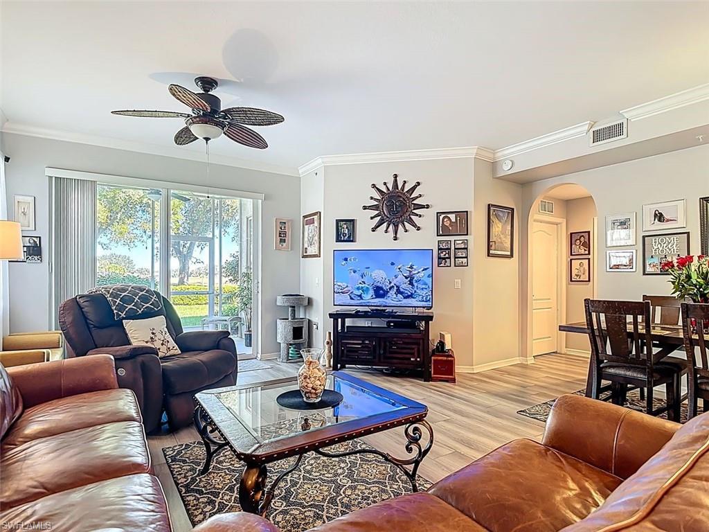 Living room with ornamental molding, arched walkways, light wood-style floors, and ceiling fan