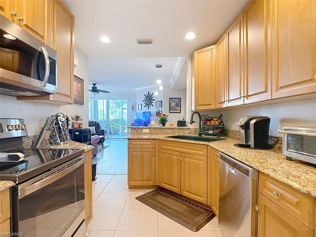 Kitchen featuring appliances with stainless steel finishes, light brown cabinetry, open floor plan, light stone countertops, and crown molding