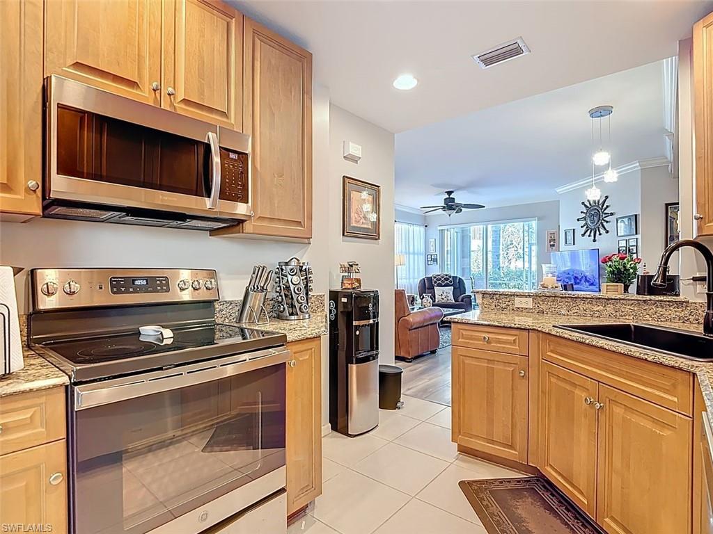 Kitchen featuring stainless steel appliances, light stone counters, open floor plan, ceiling fan, and light tile patterned floors