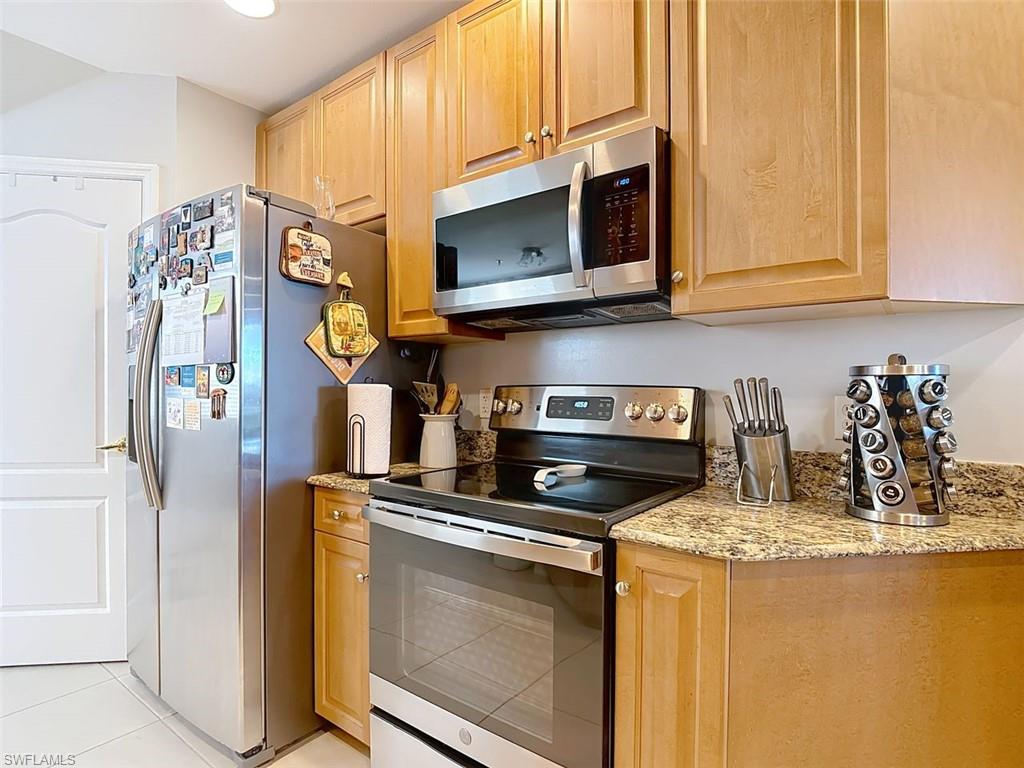 Kitchen featuring appliances with stainless steel finishes, light stone countertops, light brown cabinets, and light tile patterned floors