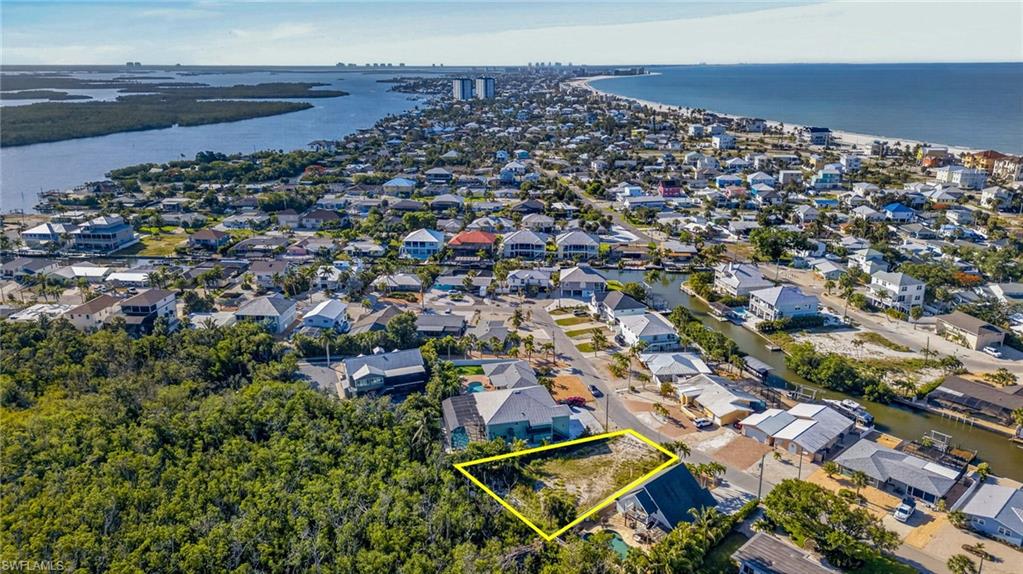 Cleared residential lot within a developed community, featuring proximity to a natural water channel, residential structures, and a sandy coastline - Virtually Edited Image