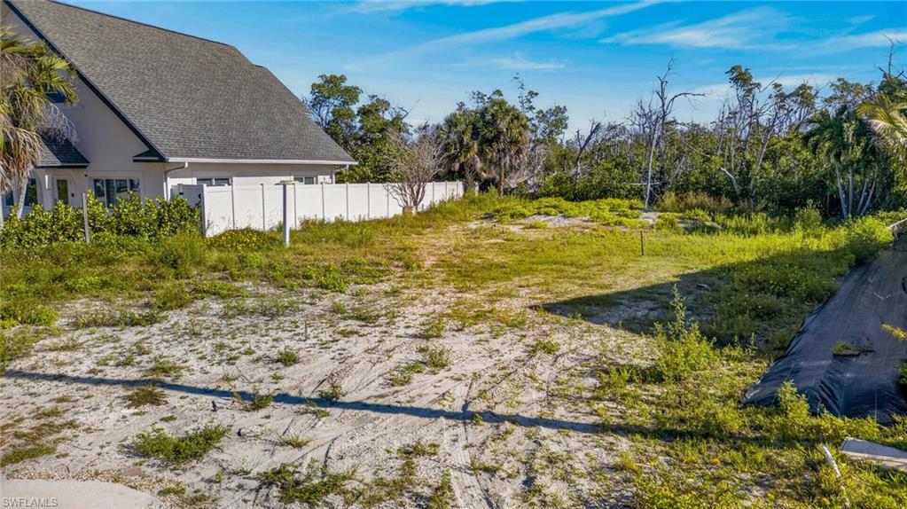 Expansive undeveloped lot featuring sandy terrain and natural vegetation, bordered by a white privacy fence - Virtually Edited Image
