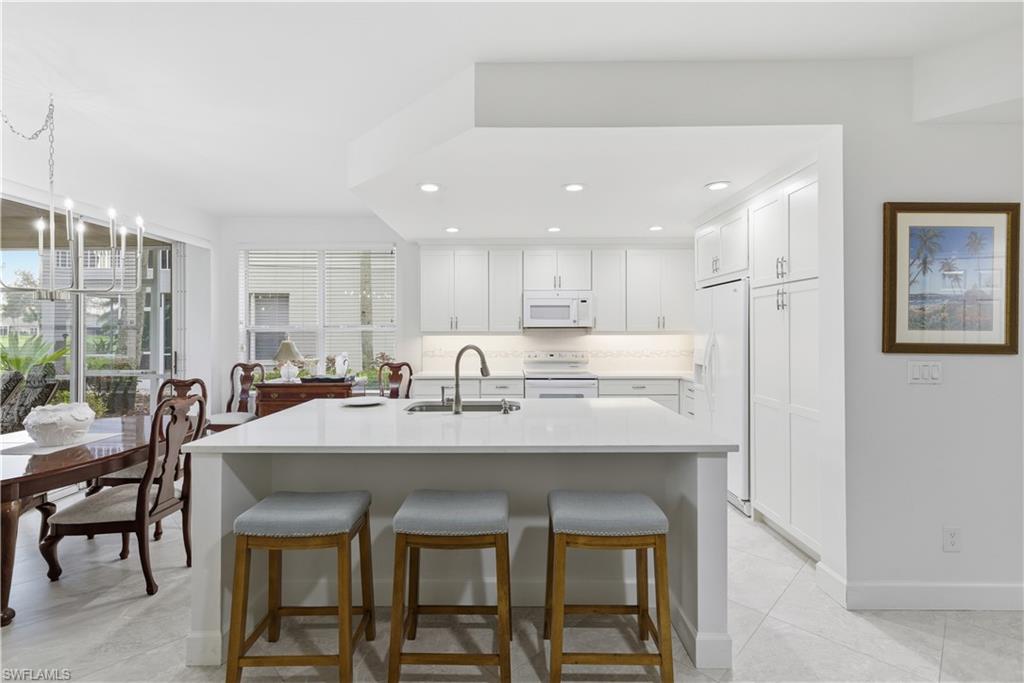 Kitchen featuring white cabinets, a breakfast bar, recessed lighting, white appliances, and light tile patterned flooring