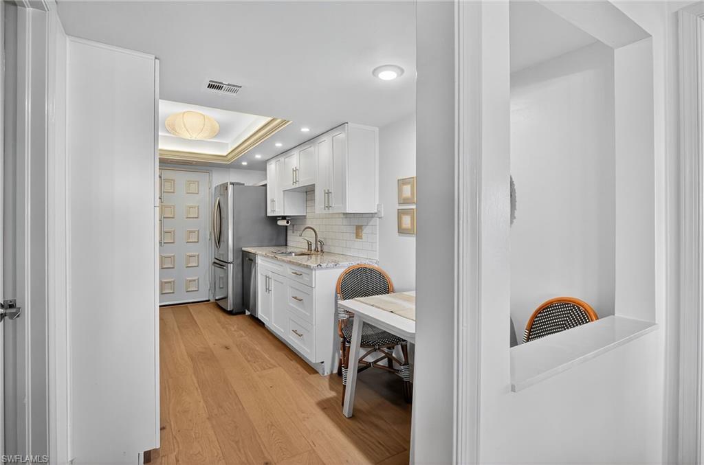 Kitchen with white cabinetry, light wood-type flooring, a raised ceiling, decorative backsplash, and recessed lighting