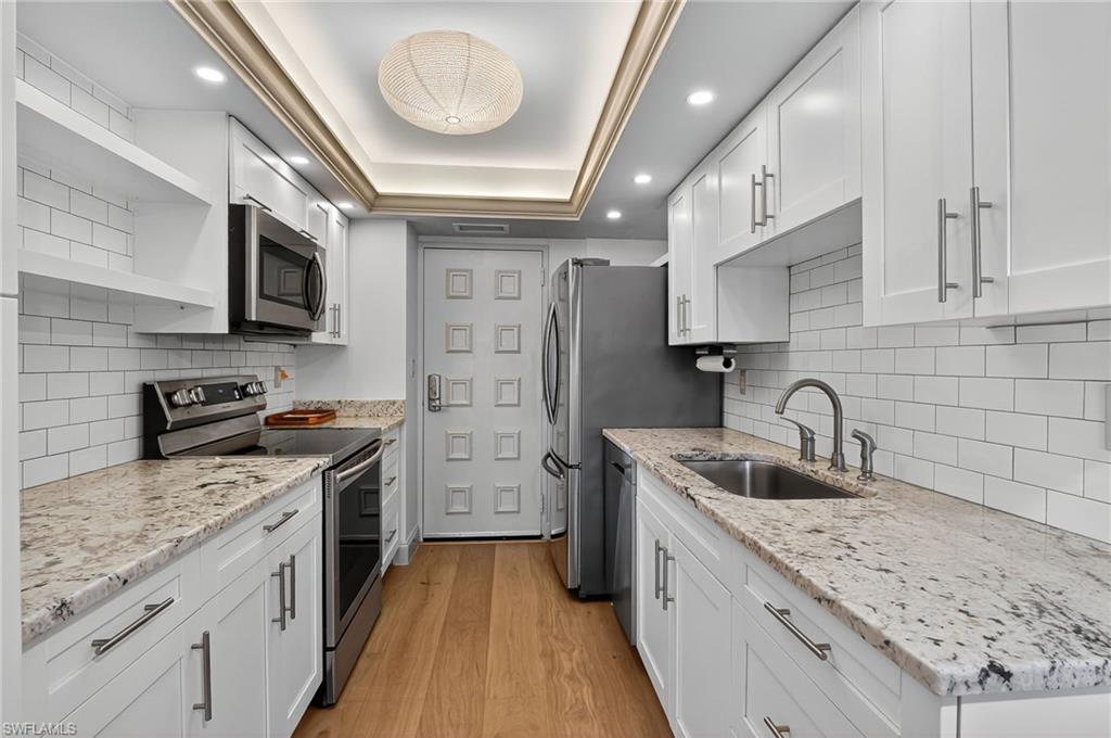 Kitchen with open shelves, stainless steel appliances, light wood finished floors, a tray ceiling, and white cabinets
