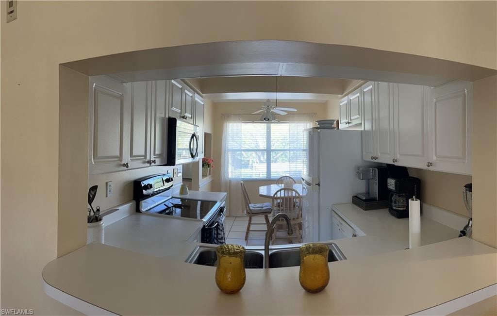Kitchen featuring an arched pass-through window, white cabinetry, a double basin sink, black appliances, and a window with horizontal blinds