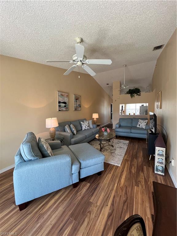 Spacious living area featuring vaulted ceilings, wood-finish flooring, and multiple ceiling fans