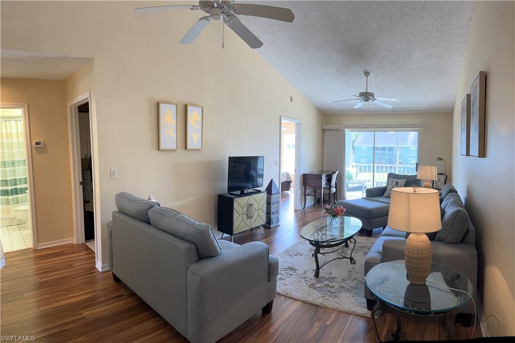 Spacious living area featuring vaulted ceilings, wood-finish flooring, and dual ceiling fans