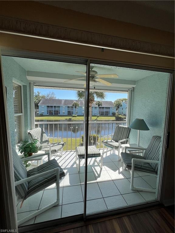 Enclosed patio featuring sliding glass doors, white tiled flooring, a ceiling fan, and a water-facing balcony with metal railings
