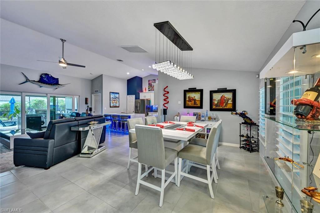 Open-concept interior featuring light gray tile flooring, a contemporary linear chandelier, vaulted ceilings, and extensive sliding glass doors