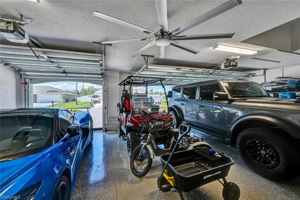 Spacious 3 car garage featuring an epoxy-coated floor, multiple automatic garage doors, and a large ceiling fan