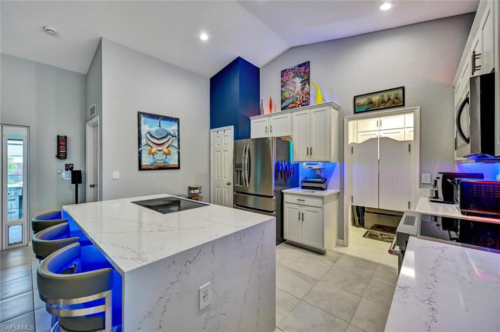 Kitchen featuring a large waterfall island with integrated cooktop, white cabinetry, stainless steel refrigerator, and tiled flooring