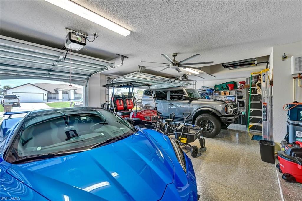 Spacious 3 car garage featuring a finished epoxy floor, large ceiling fan, and multiple overhead fluorescent light fixtures