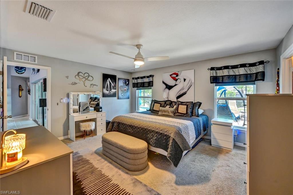 Carpeted bedroom featuring a ceiling fan, two windows with valances, a built-in vanity with mirror, and a doorway opening to an interior hallway with tile flooring