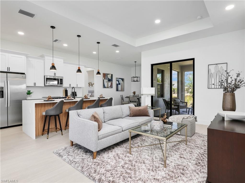 Open concept living space featuring light wood-finish flooring, a contemporary kitchen island with ribbed wood paneling, and modern pendant lighting