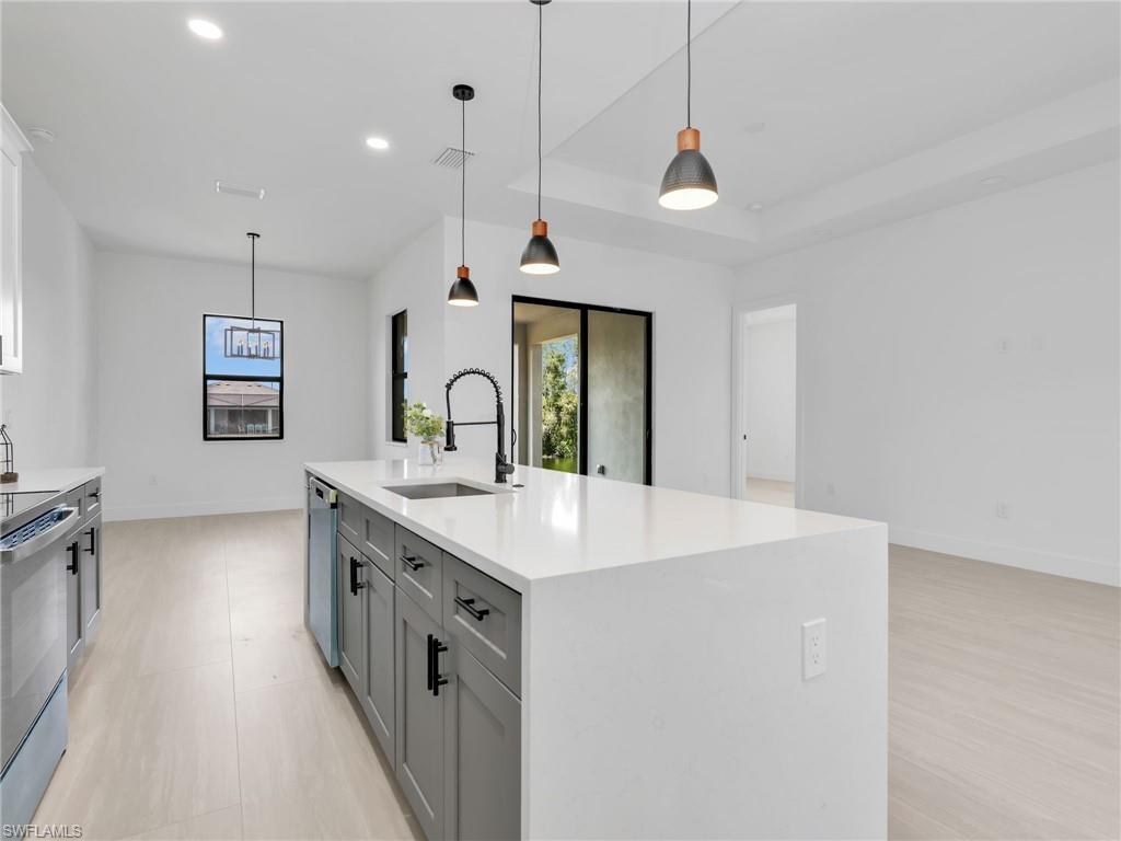 Open-concept kitchen featuring a large  island with a white solid surface countertop, matte black faucet, and gray shaker-style cabinetry
