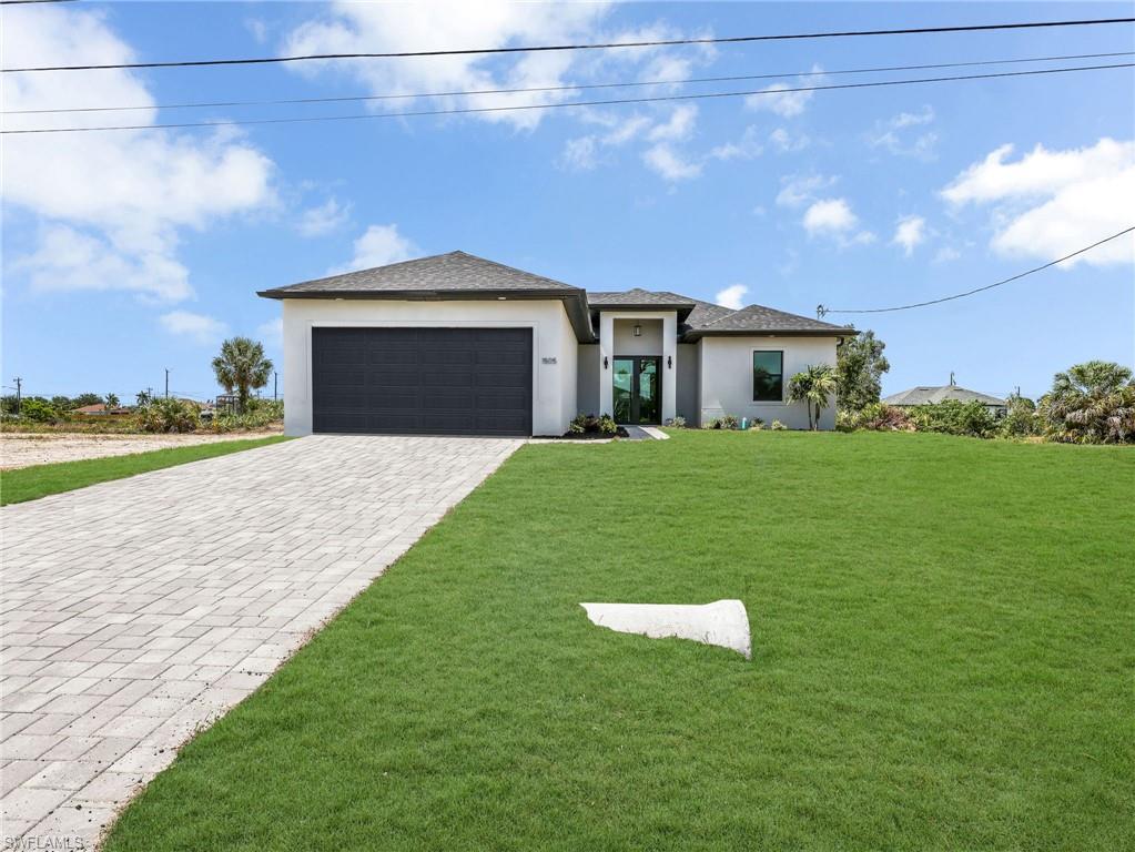 Contemporary stucco exterior with a dark shingle roof, a two-car garage with a dark panel door, a paver driveway, and a manicured front lawn
