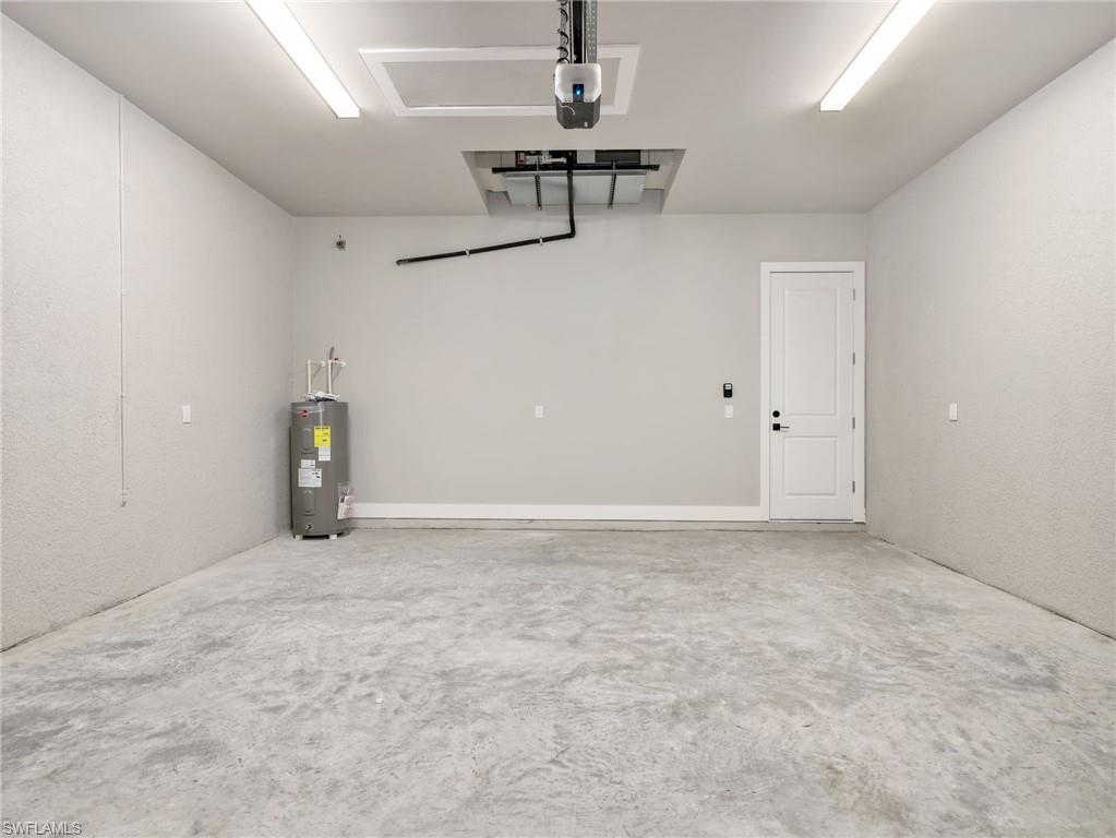 Spacious garage featuring a concrete floor, light gray walls, built-in water heater, interior access door, and overhead lighting
