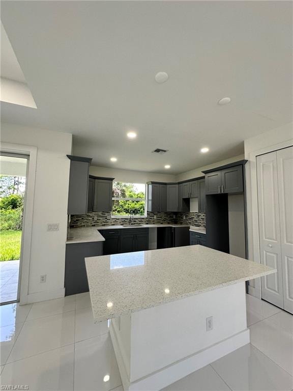 Kitchen featuring a kitchen island, light stone counters, backsplash, a kitchen bar, and light tile floors