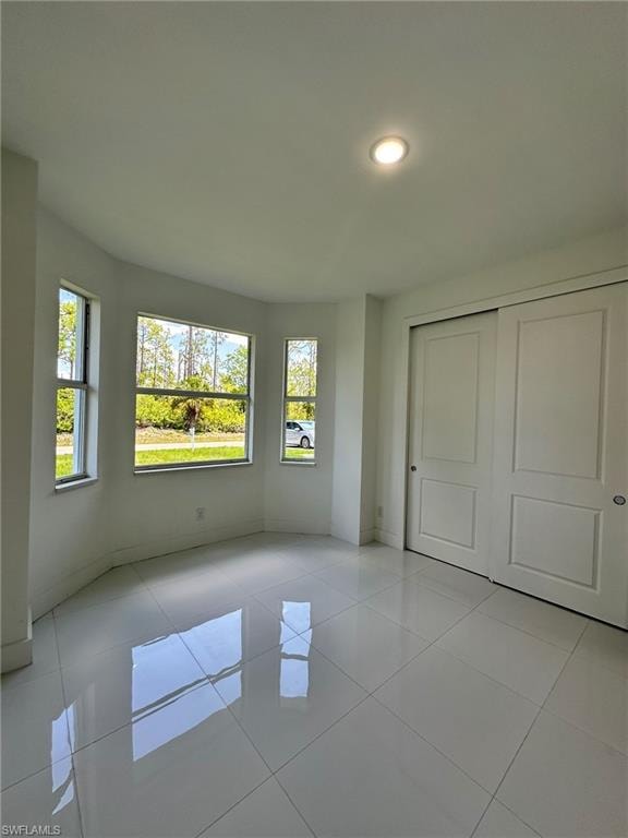 Unfurnished bedroom with a closet, light tile floors, and multiple windows