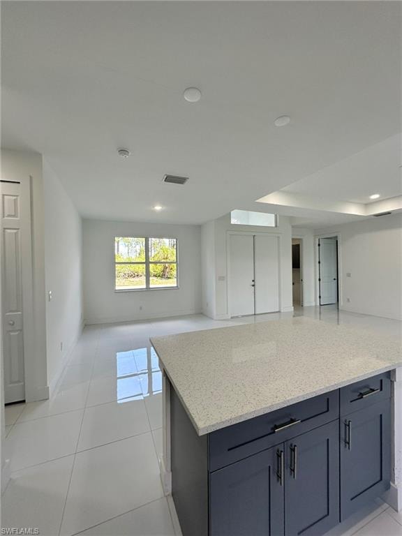 Kitchen featuring light stone countertops, light tile flooring, and a kitchen island