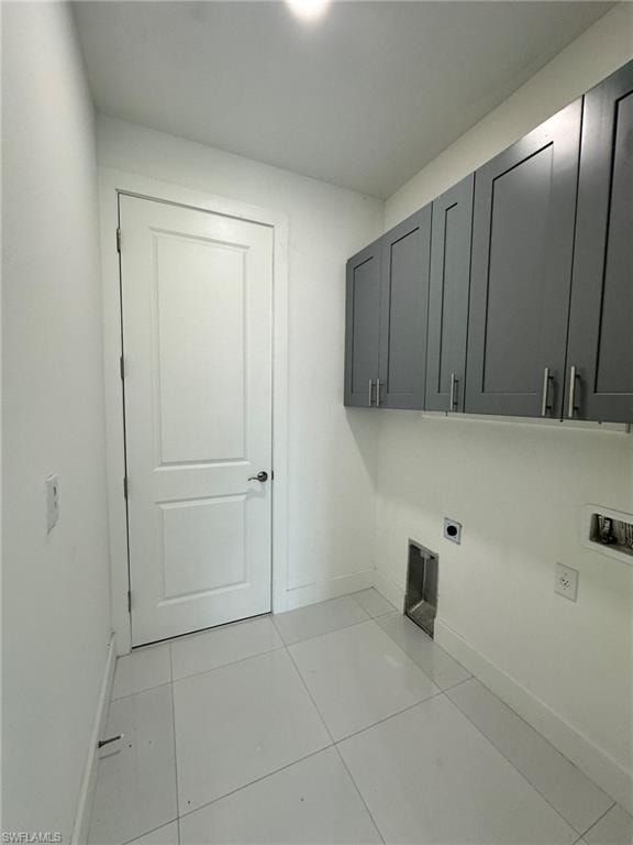 Clothes washing area with cabinets, hookup for an electric dryer, light tile floors, and washer hookup