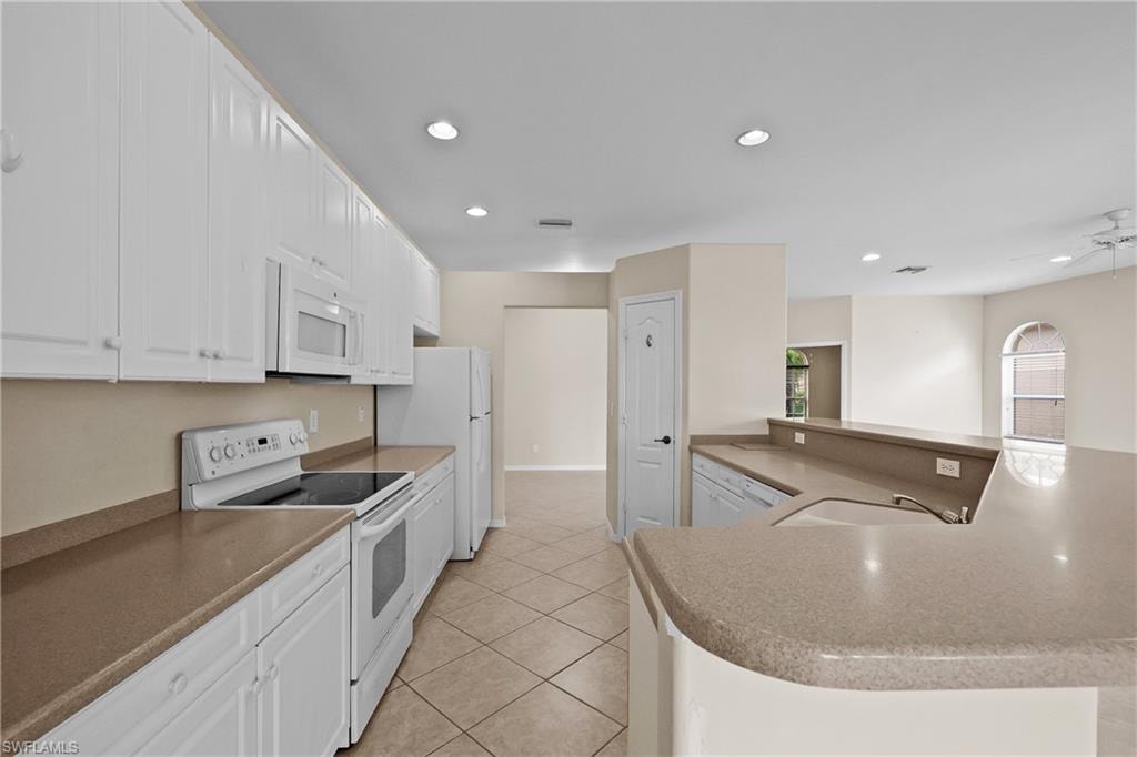 Kitchen with white appliances, white cabinets, pantry, recessed lighting, light tile patterned floors.